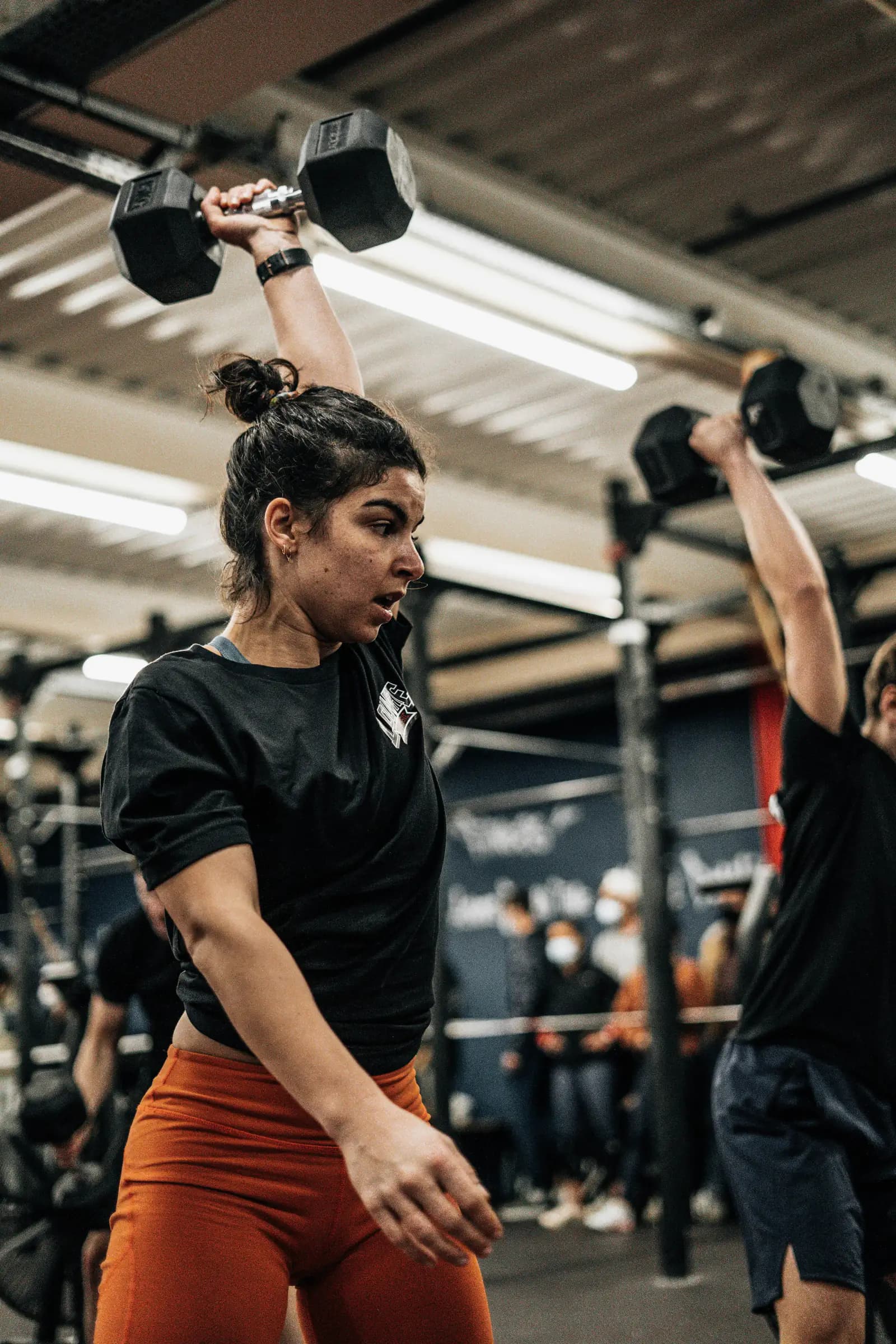 A woman pressing a dumbbell overhead during a gym workout
